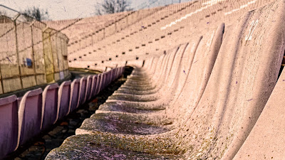 O perspectivă apropiată asupra rândurilor de scaune uzate ale stadionului Dan Păltinișanu, cu numărul 32 vizibil pe unul dintre ele, sub o lumină caldă.